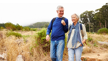 A middle aged man and woman hiking outside.