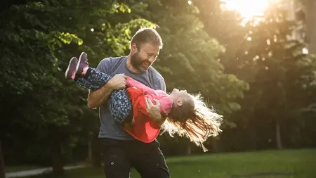 A father spinning his daughter around in a park.
