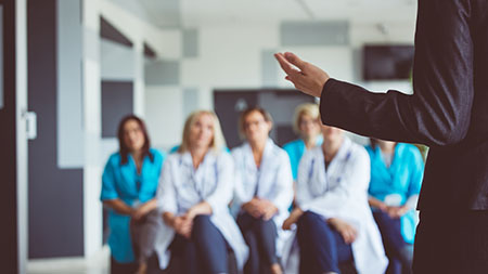A group of healthcare professionals listen to a person speaking to the group