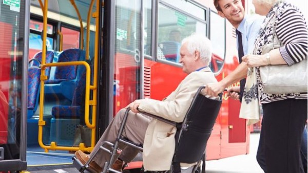 Elderly woman in wheelchair getting assistance boarding a bus