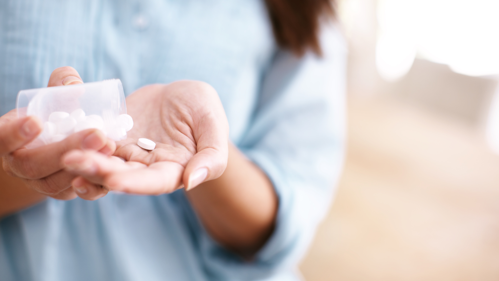 A woman in a blue shirt holds white pills in her palm