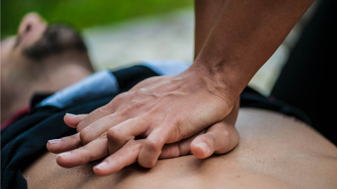 A man lies flat while someone doing CPR on his bare chest.